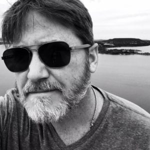 Man with sunglasses near water, grayscale photo.