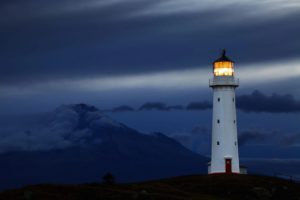 Lighthouse illuminated at night near mountain.