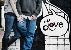 Couple standing near love-themed graffiti artwork.