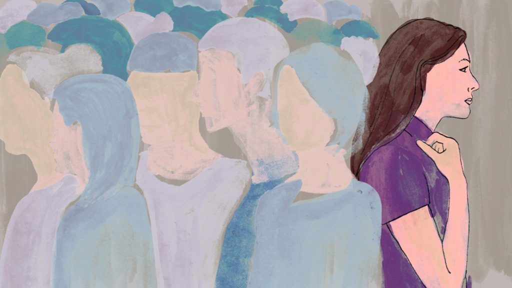 Woman standing apart from indistinct crowd.